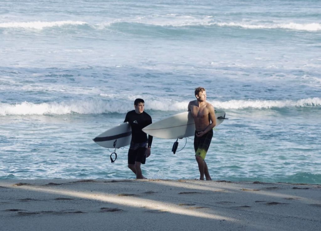 tommy and pete holding surfboards at beach